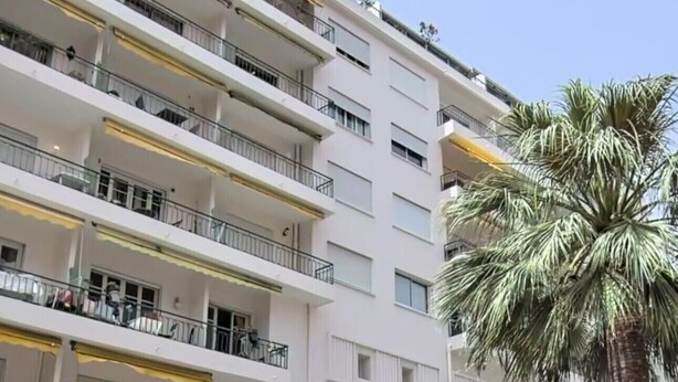 A multi-story building with balconies, a palm tree, and storefronts including a hair salon. - CIOLLI (Cannes)