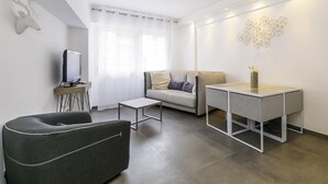 A modern living room with a sofa, a coffee table, a TV on a stand, a decorative wall piece, and a small table with a vase. - CIOLLI (Cannes)