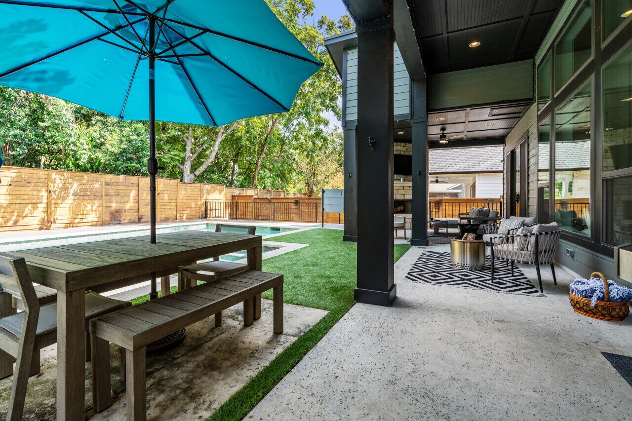 A covered patio area with a pool, wooden furniture, and a large umbrella.