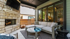 A cozy outdoor living area with a stone fireplace, a sectional sofa, and a round table.
