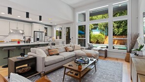 A modern kitchen with white cabinets, a stainless steel refrigerator, and a dining area with a gray sofa and coffee table.
