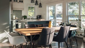 Una cocina moderna con una isla central, luces colgantes y un comedor con mesa y sillas de madera.