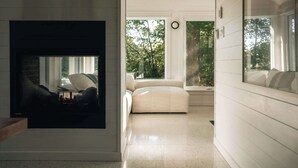 Un interior moderno con chimenea, un sofá y un ventanal con vistas a árboles.