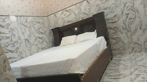 Un lit simple avec un cadre en bois foncé et du linge de lit blanc, dans une pièce dont les murs sont décorés d’un motif marbré.