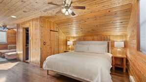 A wooden-paneled bedroom with a bed, two bedside lamps, and a ceiling fan.