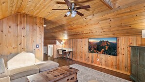 A cozy cabin interior with a wooden ceiling, a dining area, a sofa, a coffee table, and a large window with a mountain view.