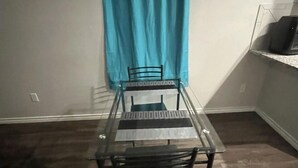 A small, enclosed room with a glass-top table and two chairs, a blue curtain, and a tiled floor.
