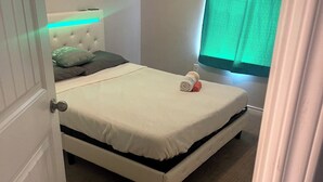 A small, neatly made bed in a room with a closed door and a window with green curtains.