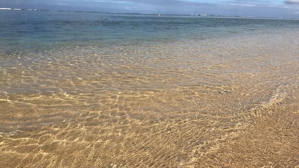 Una playa con aguas cristalinas y poco profundas, y una costa distante.