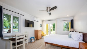 A bedroom with a bed, a desk, a chair, a television, and a ceiling fan.