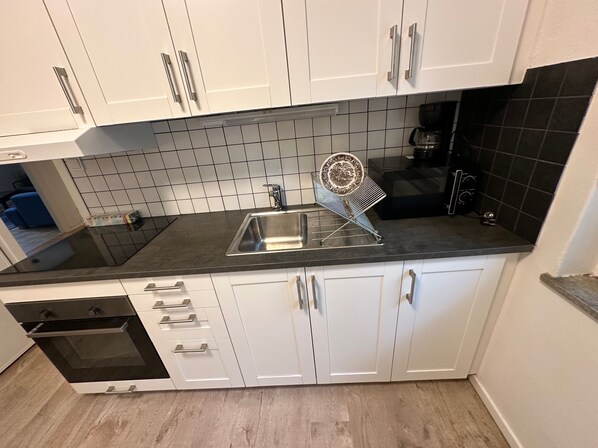A modern kitchen with white cabinets, a black countertop, and a built-in dishwasher. - Apartment Telefonplan, Stockholm (Hägersten)
