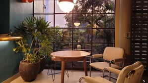 A cozy seating area with a round table and two chairs, a large potted plant, and a view through a window with a grid pattern. - w Dazzling Loft w Majestic Deco in Poblado (Medellín)