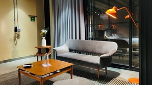 A modern hotel room with a grey sofa, a wooden coffee table, a vase with flowers, and a large window with curtains. - w Dazzling Loft w Majestic Deco in Poblado (Medellín)