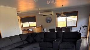 Ein Wohnzimmer mit Ecksofa, einem großen Teppich, Holzboden, Deckenventilator und einer Wanduhr.