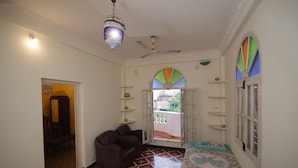 Une pièce dotée d’un ventilateur de plafond, d’un sol à motifs, d’un canapé, d’un lit recouvert d’une courtepointe colorée et offrant une vue à travers une porte.