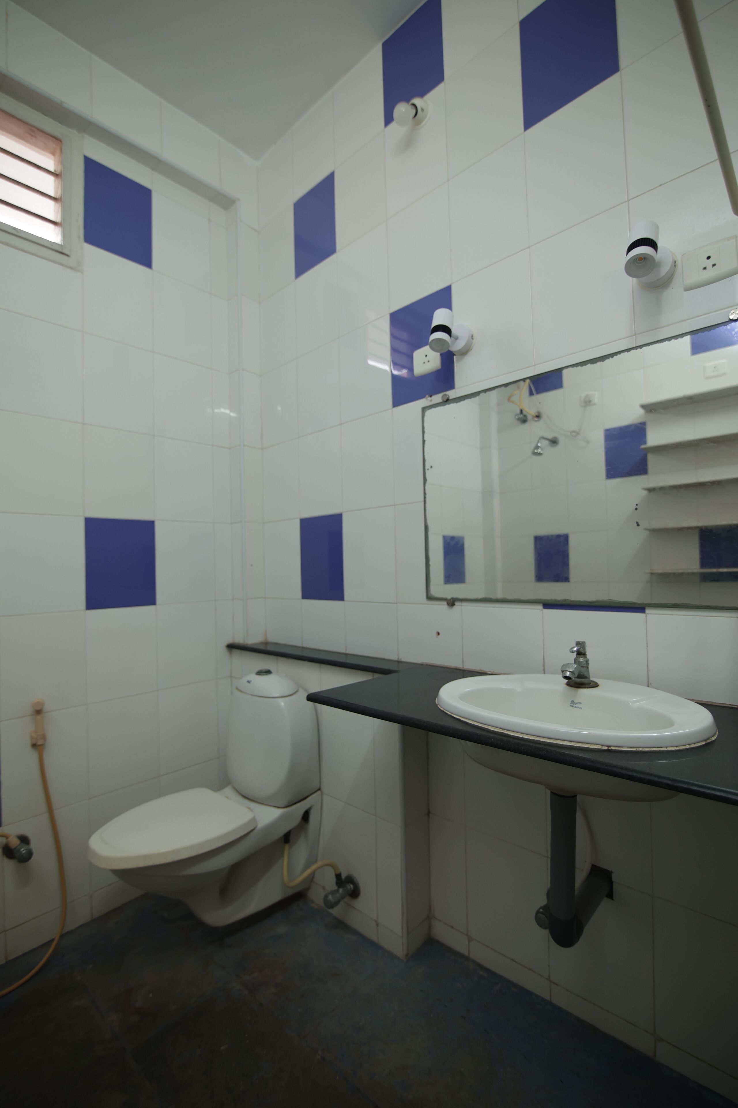 A bathroom with a toilet, sink, and mirror. There are blue tiles on the walls and a window with blinds.