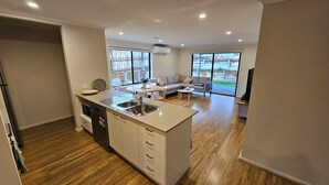 A modern kitchen with a central island, a dining area with a round table, and a living room with a sofa. - Getaway on Amaroo Way (Newborough)