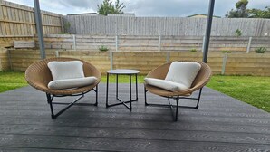 Two wicker chairs with white cushions and a small round table on a wooden deck. - Getaway on Amaroo Way (Newborough)