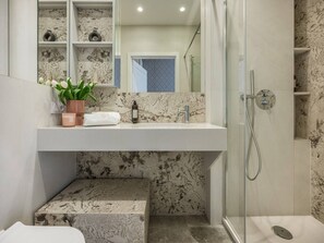 A bathroom with a marble sink, a glass shower enclosure, and a potted plant.
