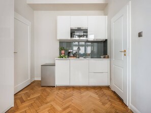 Una cucina compatta con mobili bianchi, una cappa in acciaio inossidabile e un pavimento in legno a spina di pesce.