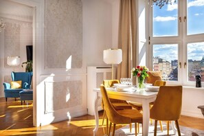 Un comedor con una mesa dispuesta para cuatro personas, un sillón azul, un sillón amarillo y una ventana con vistas a la ciudad.