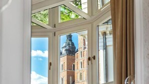 Ein Zimmer mit Erkerfenster und Blick auf ein historisches Gebäude mit einem markanten Turm.