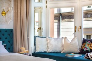 Ein Hotelzimmer mit einem türkisfarbenen, bezogenen Sofa, einem Bett mit weißem Kopfteil und einem Fenster mit Blick auf Gebäude.