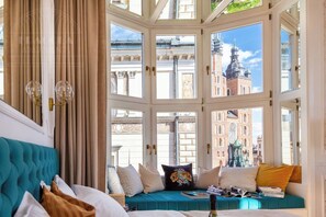 Una habitación con un amplio ventanal, un sofá color turquesa y vistas a edificios históricos.
