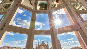 Una habitación con techos altos y varios tragaluces, vista a un edificio histórico y cielo despejado.