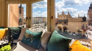 Una habitación con un amplio ventanal que da a una plaza histórica con edificios y una torre del reloj.