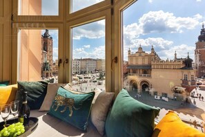 A room with a large window overlooking a historic square with buildings and a clock tower.