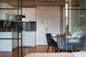 A modern kitchen with white cabinets, a stainless steel range hood, and a dining area with a glass table and two chairs.