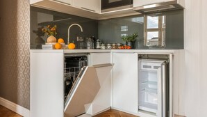 Una cocina compacta con lavavajillas, horno y refrigerador, que presenta un diseño moderno y una decoración minimalista.