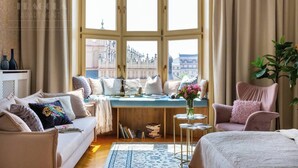 A cozy room with a bay window, a sofa, a chair, a small table with a vase, and a bookshelf. - Feniks Indigo studio with a Main Square view (Kraków - Feniks)