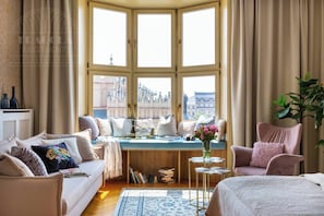 A cozy room with a bay window, a sofa, a chair, a small table with a vase, and a bookshelf. - Feniks Indigo studio with a Main Square view (Kraków - Feniks)