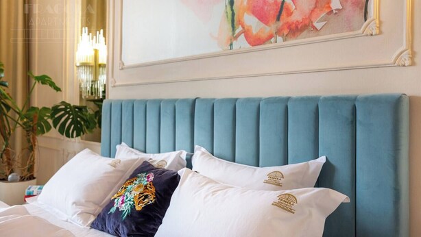 A bed with a teal upholstered headboard, white pillows, and a decorative pillow with a floral design. - Feniks Indigo studio with a Main Square view (Kraków - Feniks)
