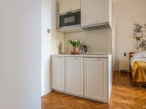 Een compact keuken met witte kastjes, een magnetron en een klein aanrecht met een plant.