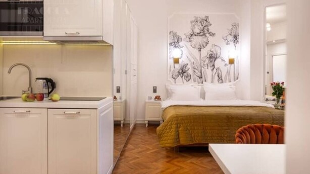 Et lille hotelværelse med tekøkken, en seng med guldgult sengetæppe og en væg med blomstermotiver.
