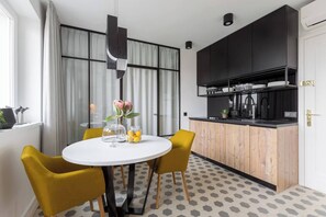 A modern kitchen with black cabinets, a white countertop, and a round dining table with yellow chairs.