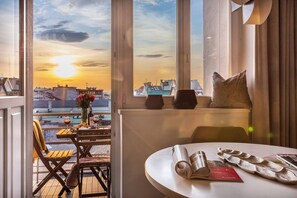 A room with a view of a sunset, a table with a book, a chair, and a window with a pillow.