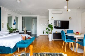 Ein modernes Hotelzimmer mit einem Bett, einer Sitzecke mit Tisch und Stühlen, einem Fernseher, einer Pflanze und einem Badezimmer mit Badewanne und Dusche.