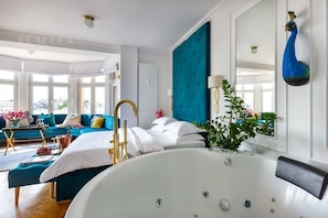 Camera d'albergo moderna con una vasca da bagno grande, una parete verde acqua e vista sulla città.
