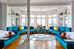 A modern living room with a blue sectional sofa, a round coffee table, and a view through large windows. - Feniks Jacuzzi Time studio (Kraków - Feniks)
