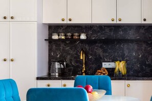 Eine moderne Küche mit Marmorfliesenspiegel, goldenen Griffen und einem blauen Stuhl.
