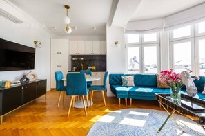 Ein modernes Wohnzimmer mit einer Couch, Sesseln, einem Esstisch und einem Fernseher.