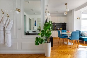A modern hotel room with a large mirror, a potted plant, a dining area with blue chairs, and a kitchen with white cabinets. - Feniks Jacuzzi Time studio (Kraków - Feniks)
