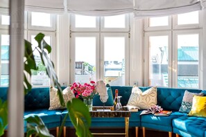 A room with a blue sofa, a glass coffee table, and a view through large windows. - Feniks Jacuzzi Time studio (Kraków - Feniks)