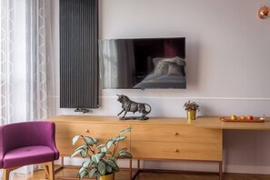 Uma sala de estar moderna com uma escrivaninha de madeira, uma cadeira roxa, uma planta em vaso, uma estátua de touro, uma televisão de tela plana e um radiador.