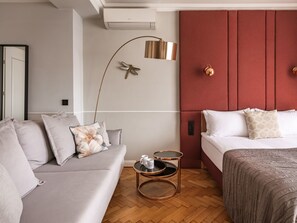 A modern bedroom with a grey sofa, a bed with a red headboard, a floor lamp, and a small round table with a cup. - Feniks Burgundy studio with a terrace (Kraków - Feniks)