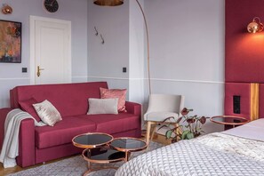 Quarto moderno com sofá vermelho, cadeira branca, mesa de centro redonda e cama com colcha branca.
